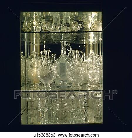Stock Image - Close up of antique glass decanters and wineglasses on glass shelves. Fotosearch