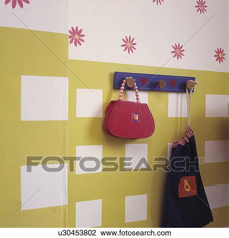 Stock Image - Close-up of bags on blue pegboard on yellow+white wall below stylised floral wallpaper&#13; &#10; &#13; &#10;. Fotosearch