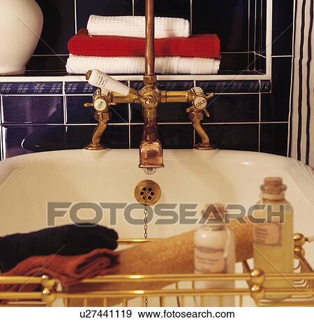 Stock Photo - Close-up of brass bath taps and rack with loofah and bath oils. Fotosearch