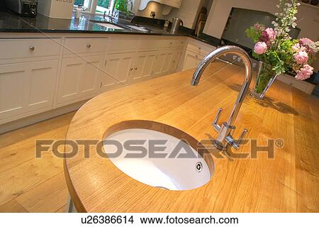 Picture - Close-up of chrome tap and white ceramic circular sink underset into wood worktop in modern kitchen. Fotosearch