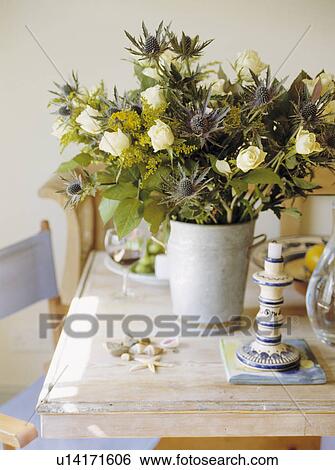 Stock Photograph - Close up of cream roses and blue eryngium in white vase on limed wood table . Fotosearch