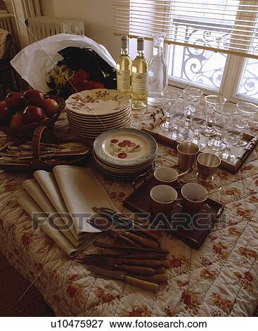 Stock Photo - Close-up of crockery and glasses with cutlery and napkins on quilted floral tablecloth. Fotosearch