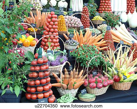 Stock Image - Close-up of display of tomatoes and carrots in pyramids and baskets with other vegetables and spices on stall in horticultural show. Fotosearch