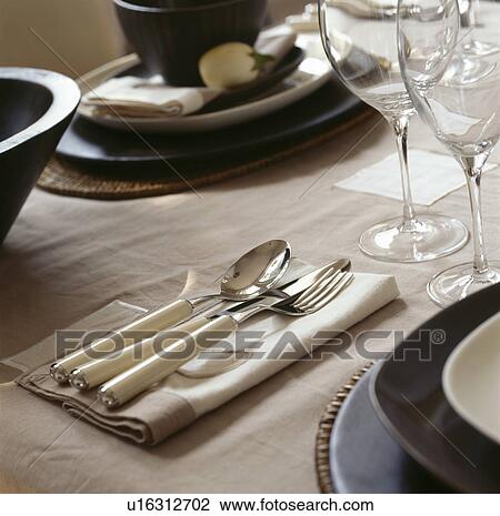 Stock Image - Close-up of glasses and cutlery with cream handles on cream linen napkin on dining table. Fotosearch