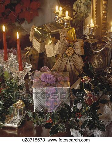 Stock Image - Close-up of gold and silver foil wrapped Christmas presents with candles and holly. Fotosearch