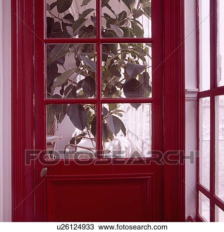 Stock Image - Close-up of half-glazed red door with view of houseplant. Fotosearch