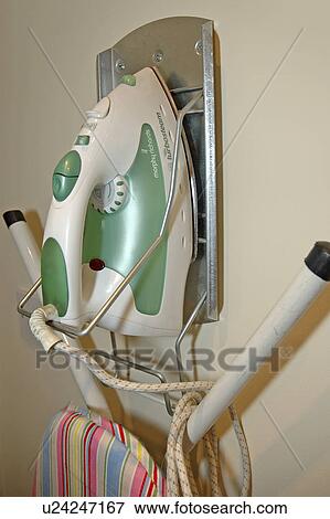 Stock Photo - Close up of iron and ironing board stored on wall rack. Fotosearch