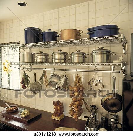 Close-up of large stainless steel and enamel pots on stainless steel shelves above hanging utensils and string of onions View Large Photo Image Stock Photo - Close-up of large stainless steel and enamel pots on stainless steel shelves above hanging utensils and string of onions. Fotosearch