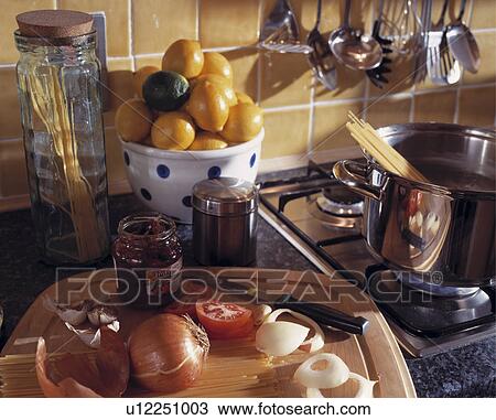 Stock Image - Close-up of lemons in bowl beside jam jar and onions on chopping board beside steel pan on hob. Fotosearch