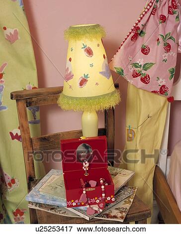 Stock Photo - Close-up of lighted fruit-patterned yellow lamp and red jewellery box on child's chair. Fotosearch