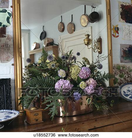 Close-up of mauve hydrangeas and green leaves in copper jug in front of large gilt mirror View Large Photo Image Stock Photograph - Close-up of mauve hydrangeas and green leaves in copper jug in front of large gilt mirror. Fotosearch