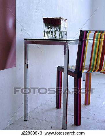 Stock Image - Close-up of multi-coloured striped perspex chair with metal table. Fotosearch