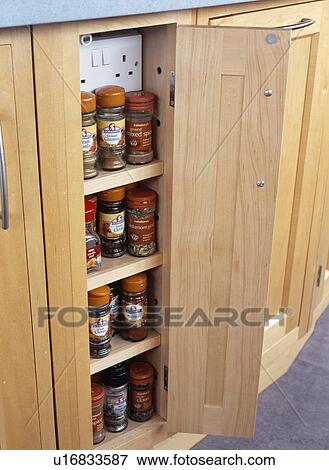 Stock Photo - Close-up of open door on cupboard with glass spice jars on shelves below electric plug sockets. Fotosearch