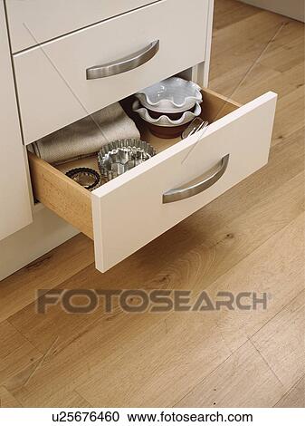 Stock Image - Close-up of open kitchen drawer above oak flooring. Fotosearch