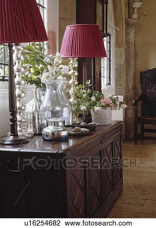 Stock Image - Close-up of pink lamps and storm lantern on carved wood antique chest. Fotosearch