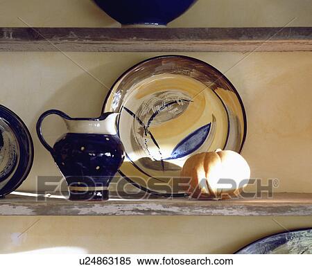 Stock Photography - Close-up of pottery jug and plate on wooden shelf. Fotosearch