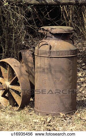 Stock Photograph - Close-up of rusty milk churn and cartwheel. Fotosearch