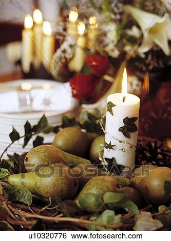 Stock Photograph - Close-up of simple Christmas decoration of white candle in basket of green pears with trailing ivy. Fotosearch