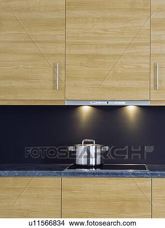 Picture - Close-up of stainless steel pan on hob below pale wood kitchen cupboard with concealed lighting&#13; &#10; &#13; &#10; &#13; &#10; &#13; &#10; &#13; &#10; &#13; &#10;. Fotosearch