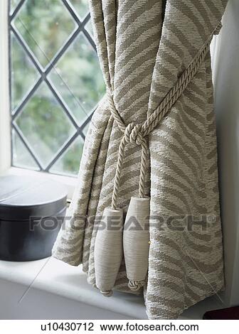 Stock Image - Close-up of striped curtain with cream rope tiebacks. Fotosearch