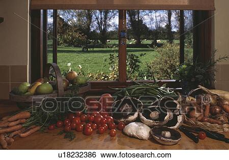 Stock Photograph - Close-up of tomatoes with mushrooms, onions and carrots on worktop below kitchen window. Fotosearch