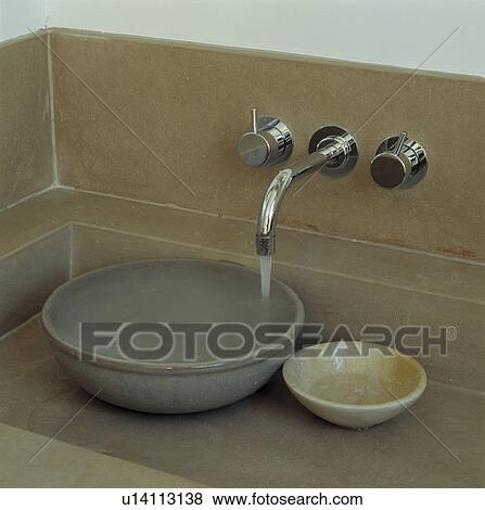 Stock Photo - Close-up of water pouring from stainless steel tap into beige ceramic bowl. Fotosearch