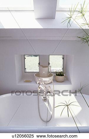 Stock Photography - Close-up of white jug and bowl on windowsill of small alcove window above white bath. Fotosearch