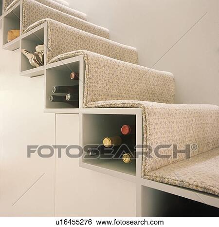 Stock Photograph - Close-up of wine stored below each stair of modern staircase with beige carpet. Fotosearch