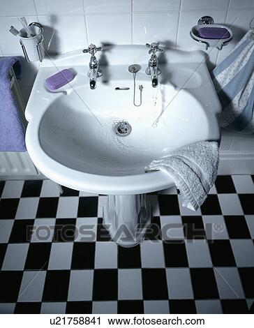 Stock Image - Closeup of black and white tiled bathroom with white basin. Fotosearch