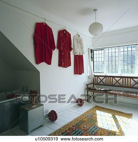 Stock Photo - Clothes on the wall above weights in white bathroom with wooden settle below the window. Fotosearch