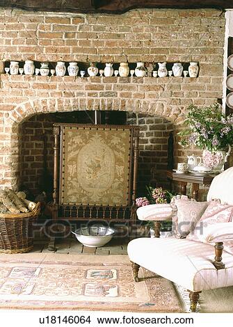 Collection of china in alcove on brick wall above fireplace with tapestry firescreen in cottage living room View Large Photo Image Picture - Collection of china in alcove on brick wall above fireplace with tapestry firescreen in cottage living room . Fotosearch