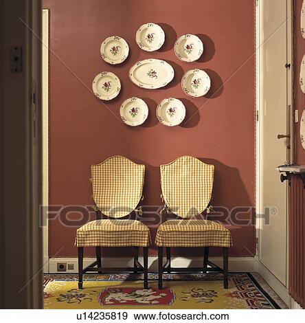 Collection of floral plates on terracotta wall above antique chairs with cream checked loosecovers View Large Photo Image Stock Photo - Collection of floral plates on terracotta wall above antique chairs with cream checked loosecovers. Fotosearch
