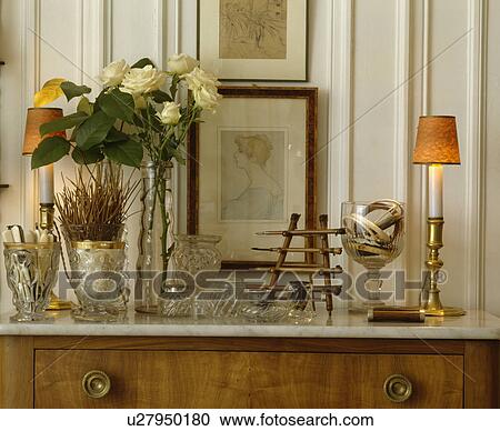 Stock Image - Collection of pressed glass vases and cream roses with pictures and lighted lamp. Fotosearch