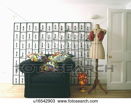 Stock Image - Colourful cushions on black armchair in front of metal screen in modern livingroom with antique tailor's mannequin. Fotosearch