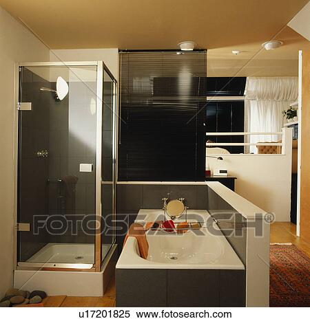 Stock Photography - Compact ensuite bathroom with shower and bath divided from bedroom by black slatted blind . Fotosearch