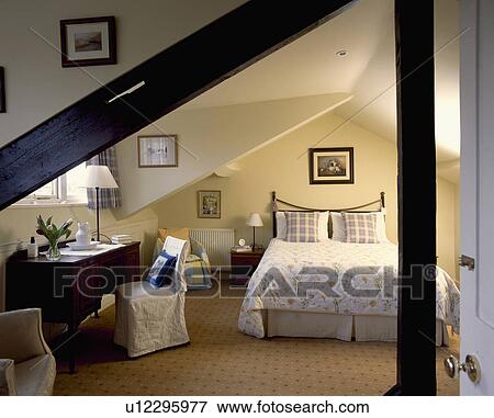 Converted attic bedroom with floral quilt on bed and loosecover on chair beside desk View Large Photo Image Stock Photo - Converted attic bedroom with floral quilt on bed and loosecover on chair beside desk. Fotosearch