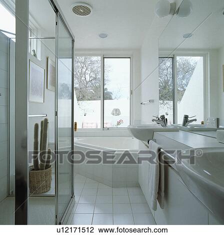 Corner bath below windows in modern white bathroom with white ceramic tiled floor View Large Photo Image Stock Image - Corner bath below windows in modern white bathroom with white ceramic tiled floor. Fotosearch