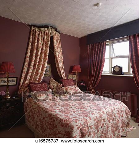 Coronet With Red White Drapes Above Bed With Matching Bedlinen In Red Bedroom With Red Curtains And Textured Ceiling Stock Photo