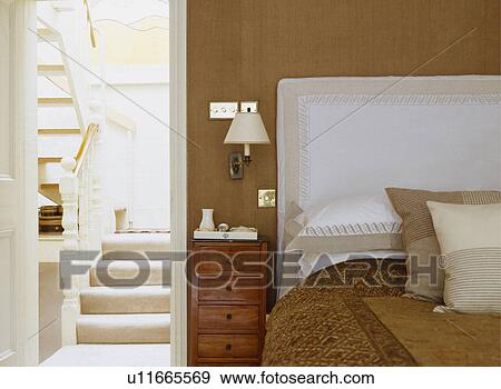 Stock Photo - Cream and white cushions and linen with matching headboard on bed beside open door to staircase. Fotosearch