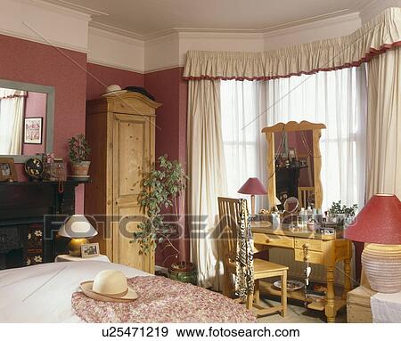 Stock Photo - Cream curtains and pine wood dressingtable and chair in red bedroom with pine wardrobe. Fotosearch