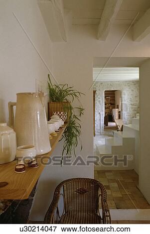 Stock Photo - Cream jug and novelty eggcup on wooden shelf in white cottage hall with open doorway to staircase. Fotosearch