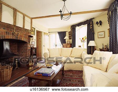 Stock Photo - Cream sofas and wooden coffee table in traditional cottage livingroom with brick fireplace. Fotosearch
