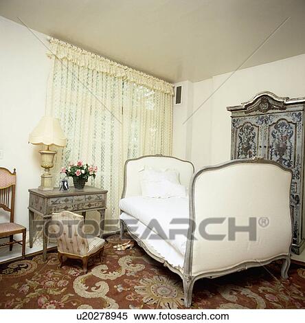 Cream upholstered Empire-style bed in traditional bedroom with lace curtains and patterned carpet View Large Photo Image Stock Photography - Cream upholstered Empire-style bed in traditional bedroom with lace curtains and patterned carpet. Fotosearch