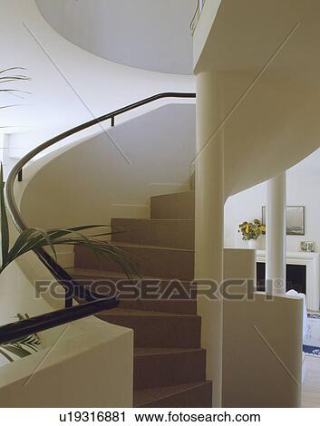 Stock Image - Curved white staircase with black handrail on solid bannister wall. Fotosearch