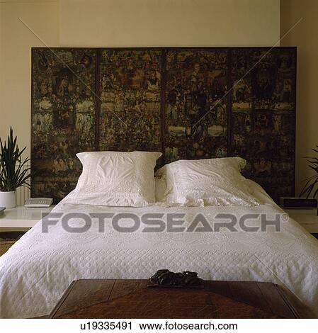Stock Image - Decoupaged Victorian folding screen behind bed with white pillows and quilt. Fotosearch
