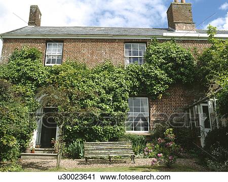 Stock Image - Detached Victorian house with green climbing plant. Fotosearch