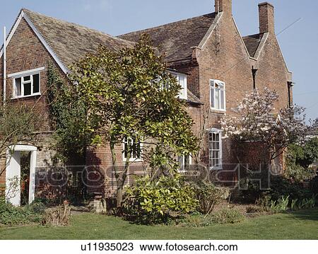 Stock Image - Detached Victorian red brick house with small trees on the lawn. Fotosearch
