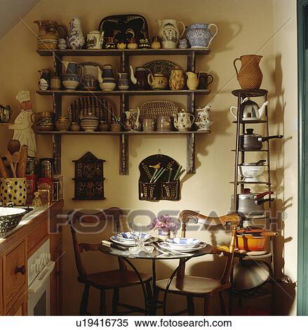 Stock Photography - Detail of small table and chairs in yellow kitchen with numerous jugs and pand on display . Fotosearch