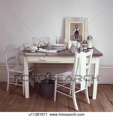 Stock Image - Detail, stainless steel topped white table and chairs in white room with wooden floor. Fotosearch