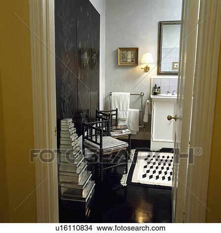 Door open to traditional black+white bathroom with stacked set of tin storage boxes beside inlaid antique chair View Large Photo Image Picture - Door open to traditional black+white bathroom with stacked set of tin storage boxes beside inlaid antique chair. Fotosearch